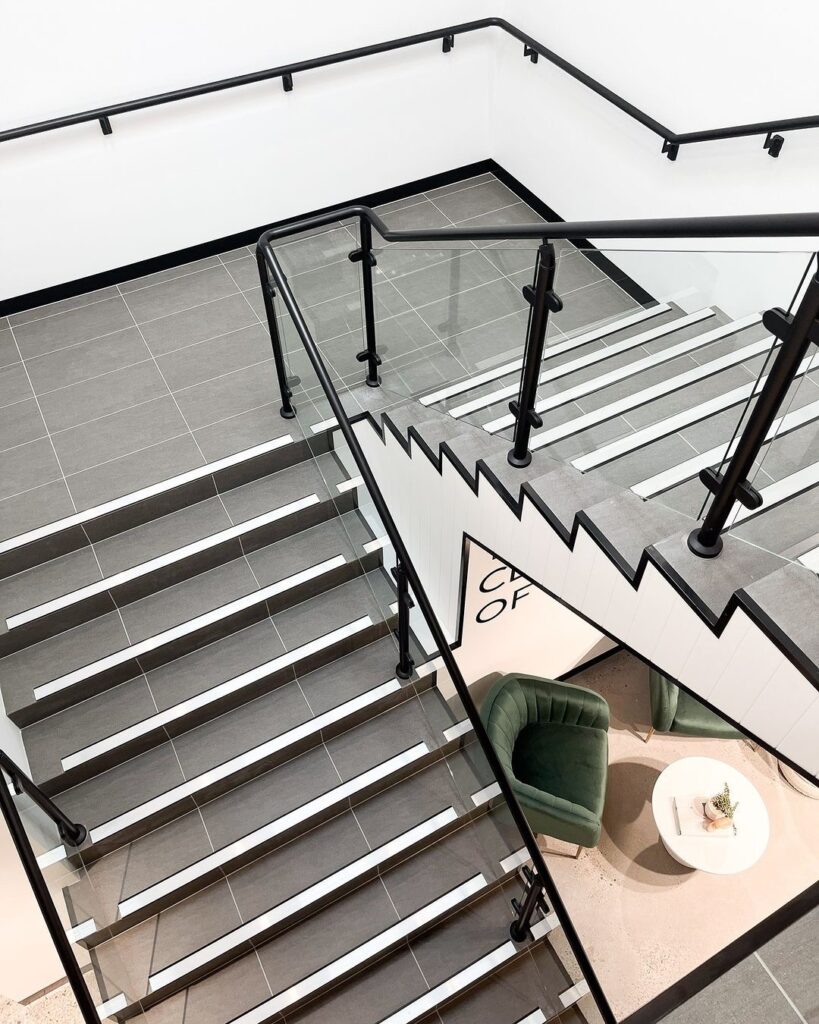 Open-concept modern office staircase showcasing tile treads and glass guardrailing.