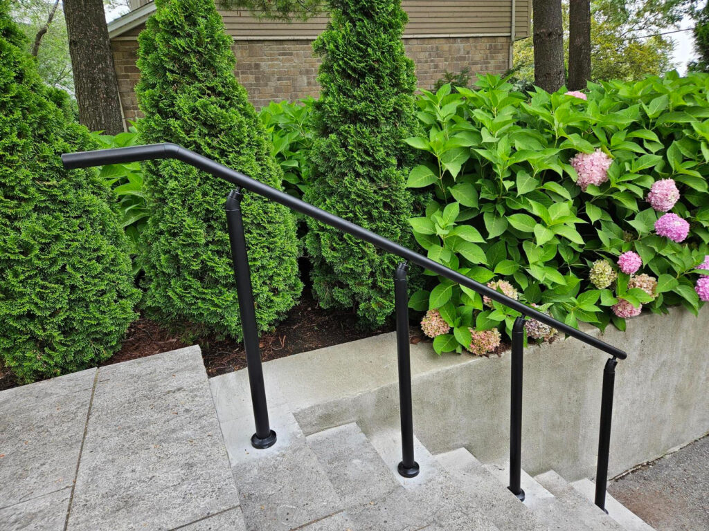 Outdoor steps with black exterior handrail system by garden.